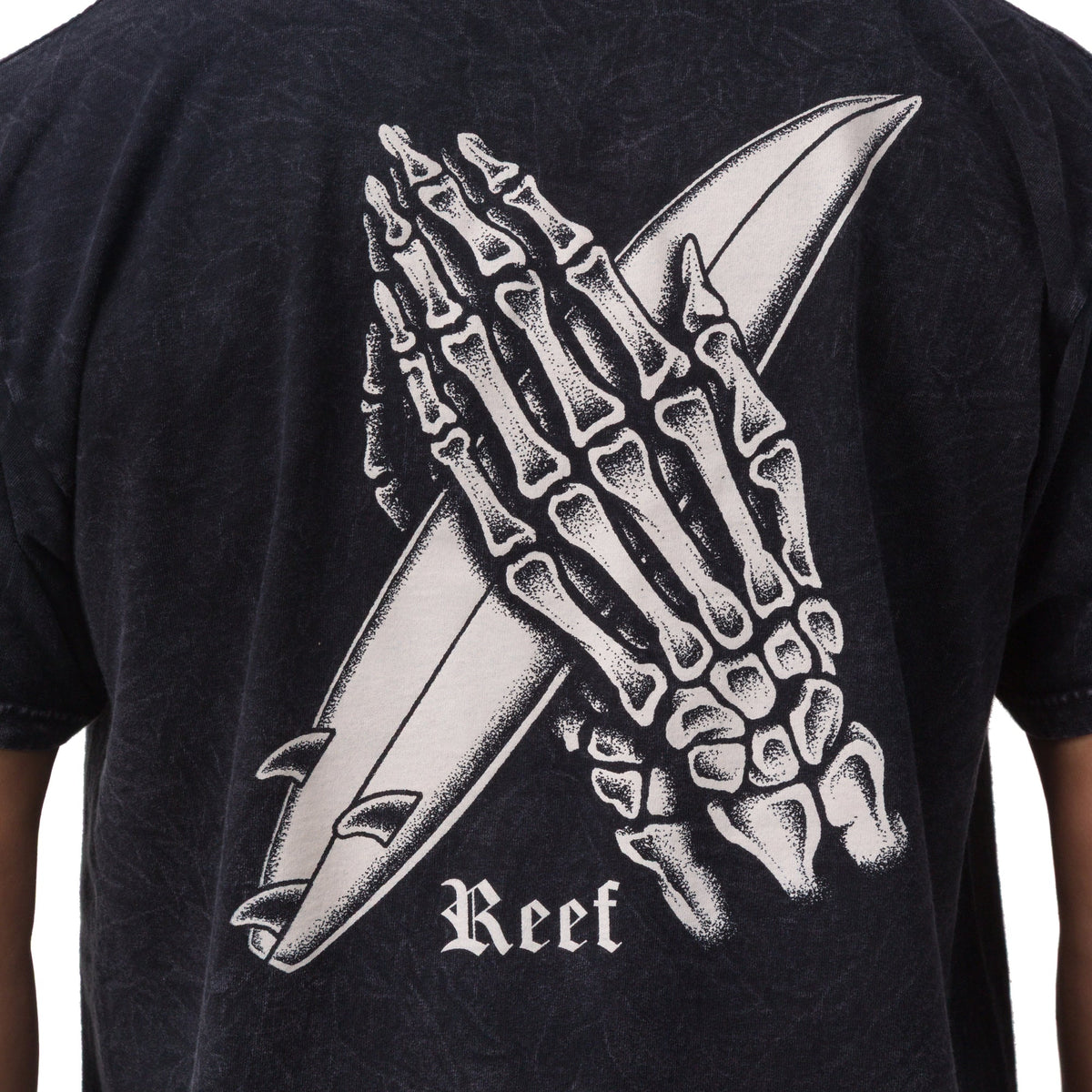 Close-up of the back of the Pray Tee showing a skeleton hand holding a surfboard print on black fabric.