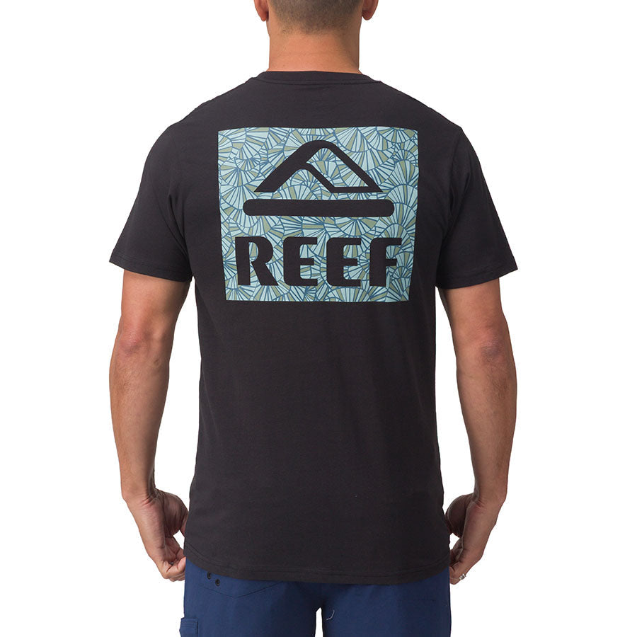 Rear view of men's Shells Tee in black with large REEF logo on blue patterned background, beach-inspired comfort apparel.