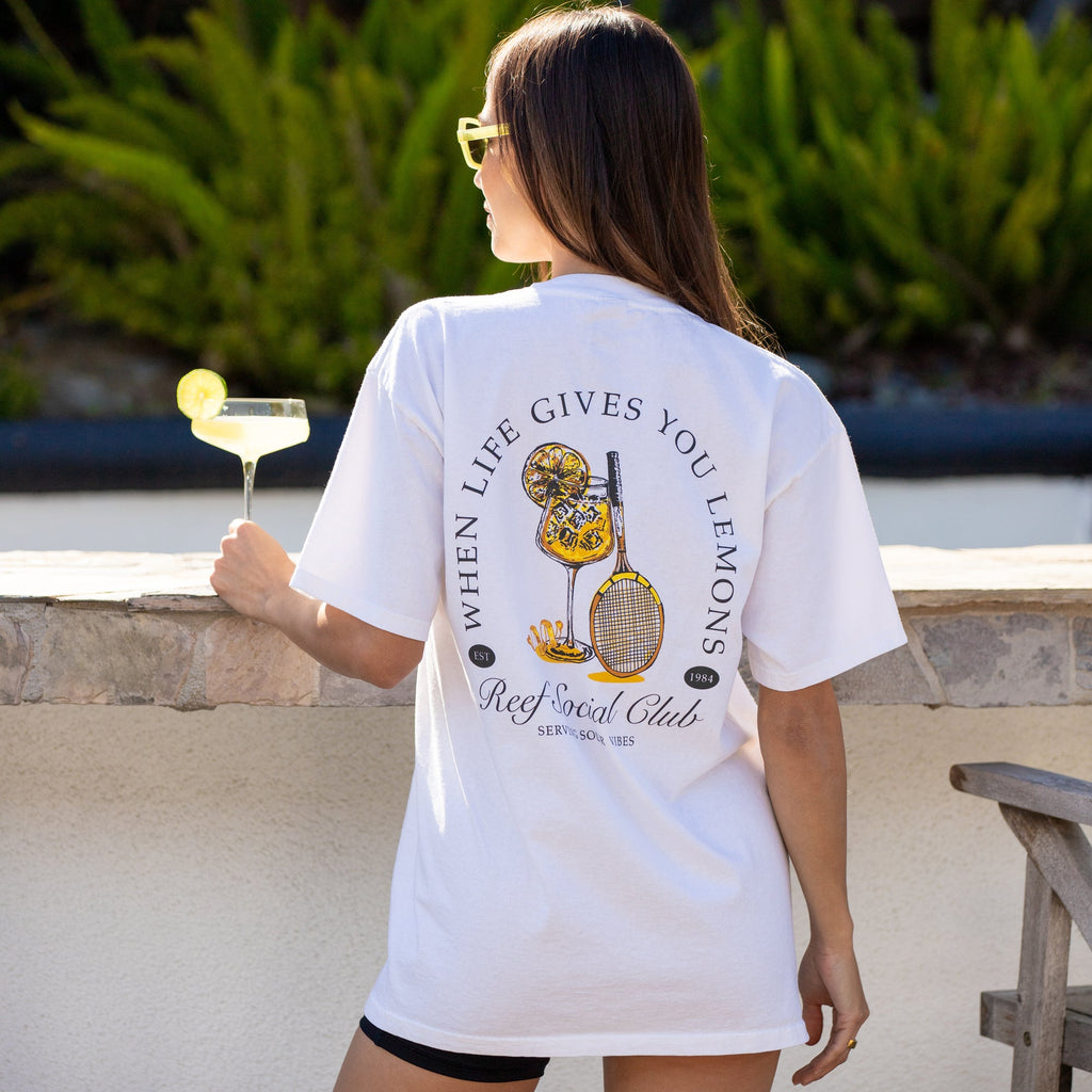 Woman wearing Social Boyfriend Crew t-shirt showing back graphic design, standing outdoors with drink in hand