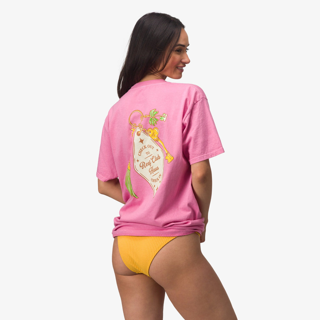 Woman wearing a pink Haus Boyfriend Crew shirt facing backward, showcasing the back design in a relaxed beach style.
