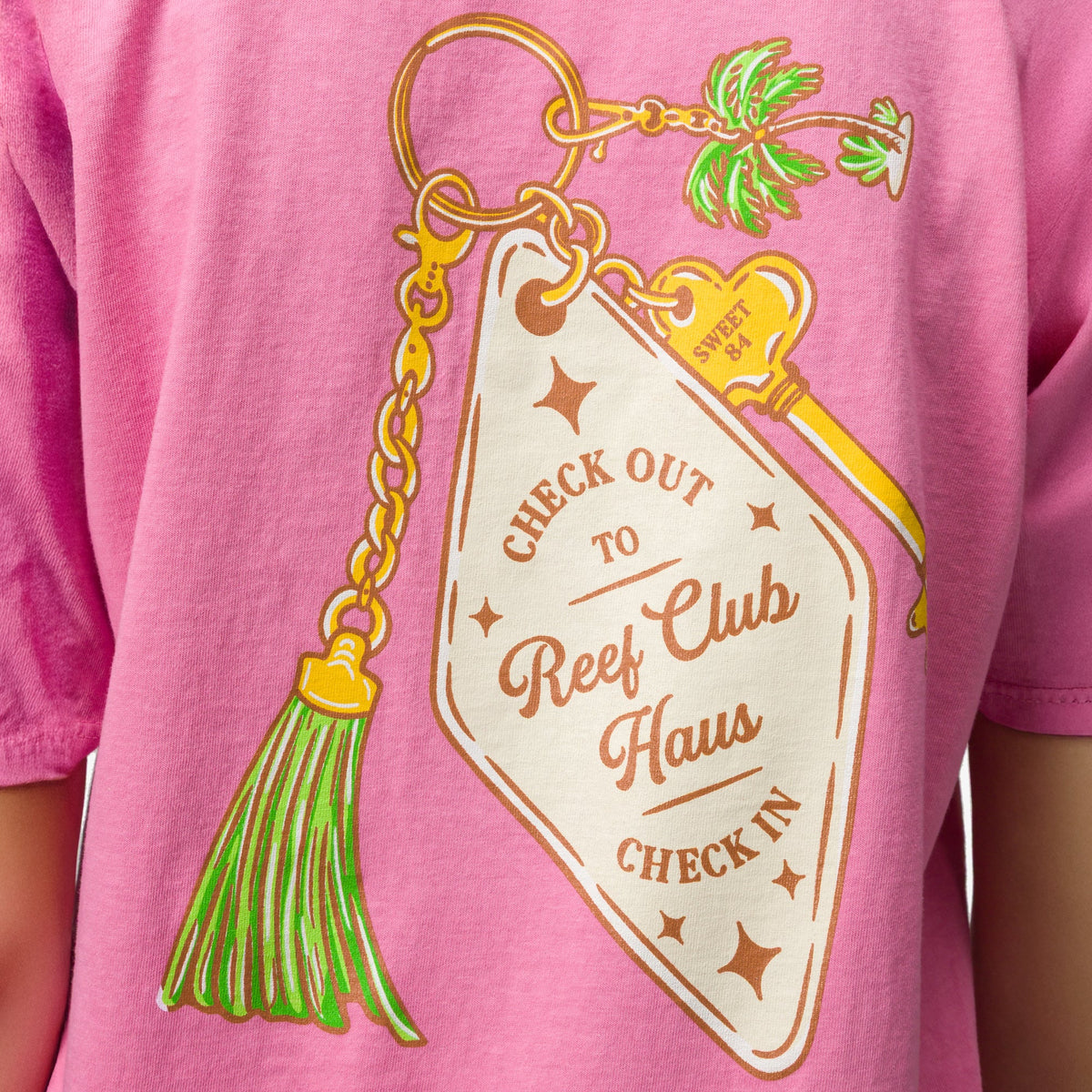 Close-up of the pink Haus Boyfriend Crew shirt back featuring a colorful surf-inspired keychain graphic with palm tree and tassel.
