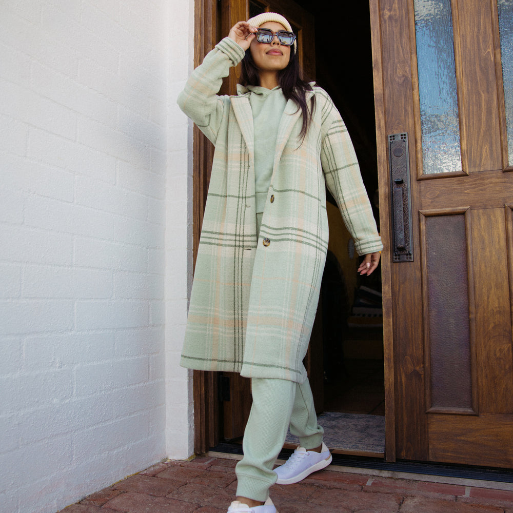 Woman wearing a desert sage plaid Beverly Knit Trench facing forward, styled for beach-inspired comfort and active lifestyles.