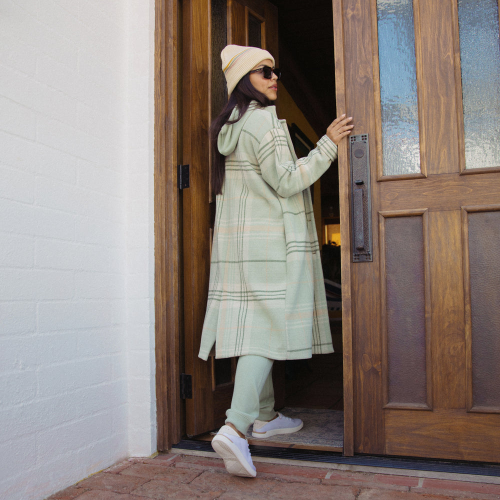 Woman wearing Beverly Knit Trench in desert sage plaid facing away, opening door, showing back and side of coat
