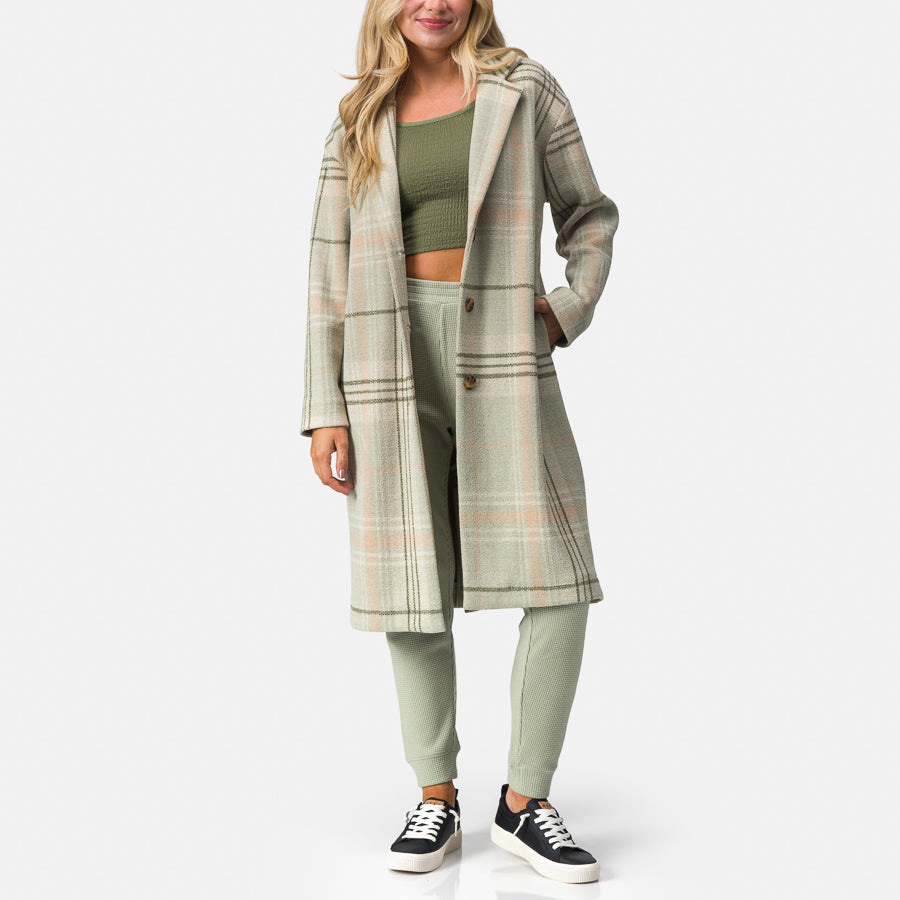 Woman wearing Beverly Knit Trench in desert sage plaid, facing front, showcasing long plaid trench coat with relaxed fit.