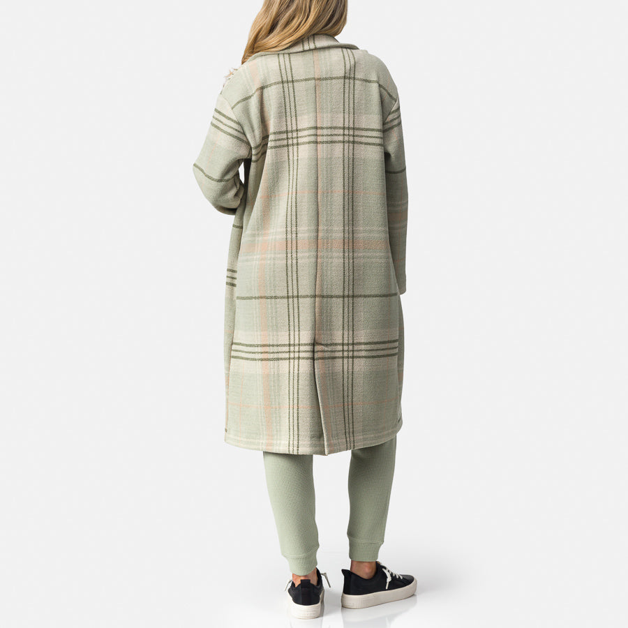 Woman wearing a desert sage plaid Beverly Knit Trench shown from back, paired with casual sneakers facing right, comfort-focused design.