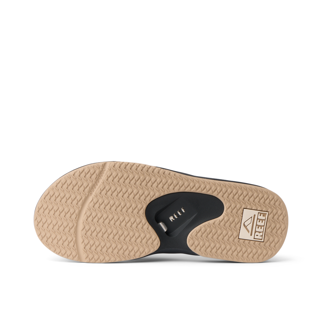 Fanning men's flip flop outsole facing up, brown herringbone tread with black bottle opener and REEF logo for beach comfort