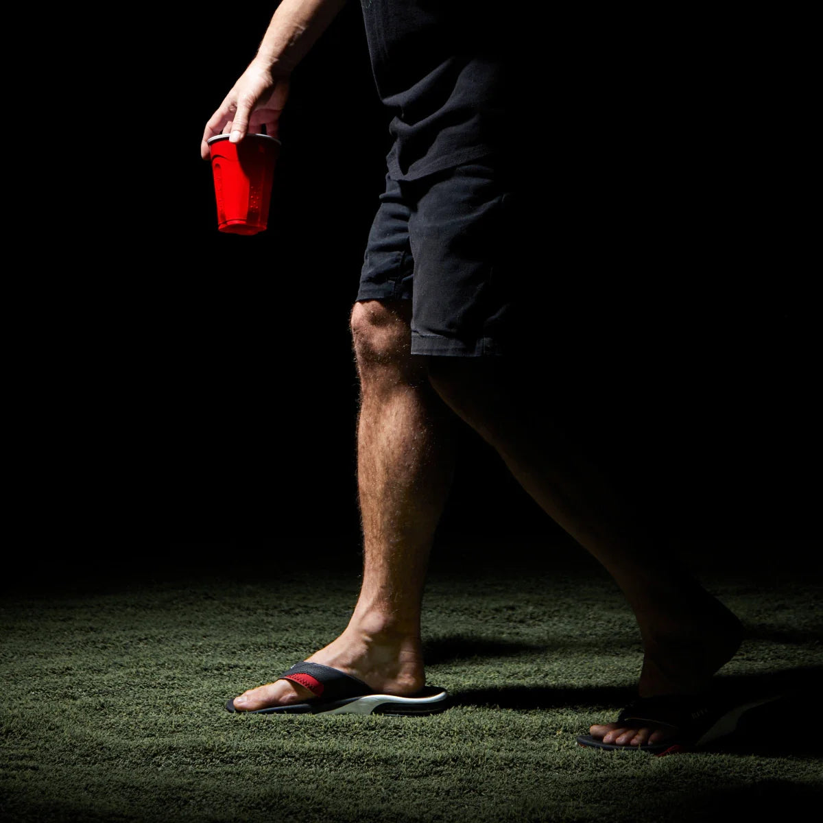 Side view of a man's feet wearing black and red Fanning Pregame sandals, showcasing comfort and surf-inspired design.