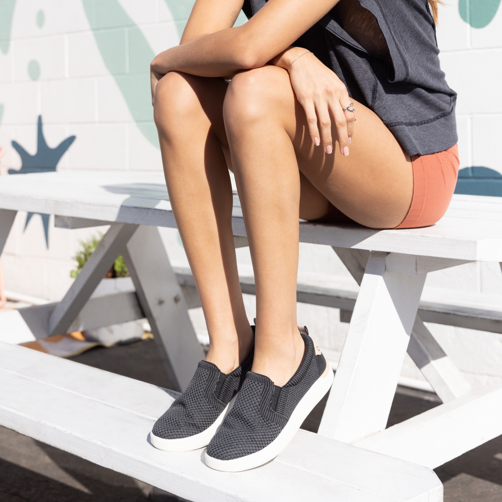 Neptune Elyse men's right shoe facing forward, close-up of black slip-on sneaker with cushioned arch support on bench.