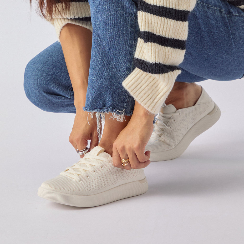 Woman wearing Reef Neptune sneakers in cream knit, right shoe facing left, close-up on lacing and upper toe area.