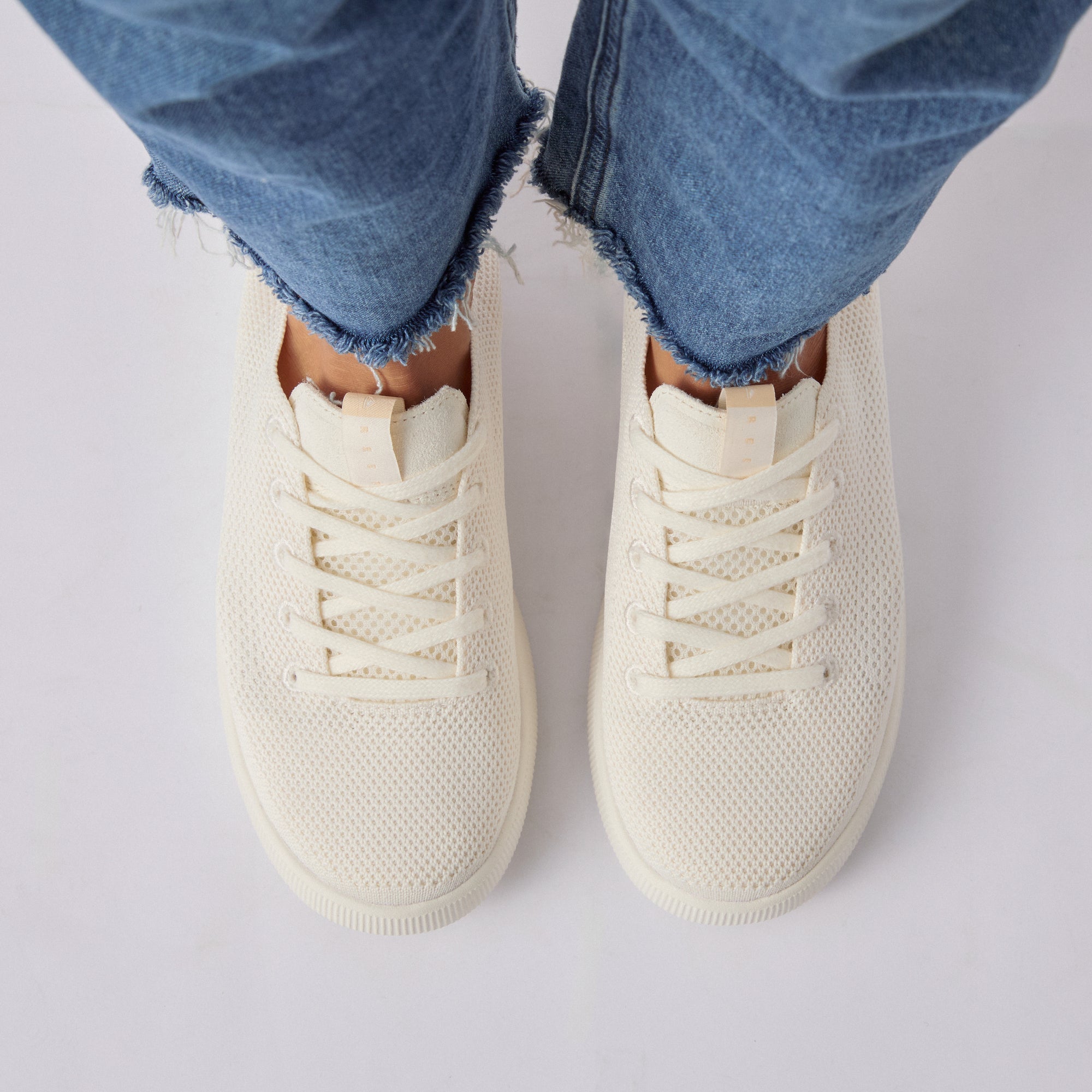Top view of women's Reef Neptune cream knit sneakers worn with blue frayed hem jeans, featuring comfort and water-friendly design.