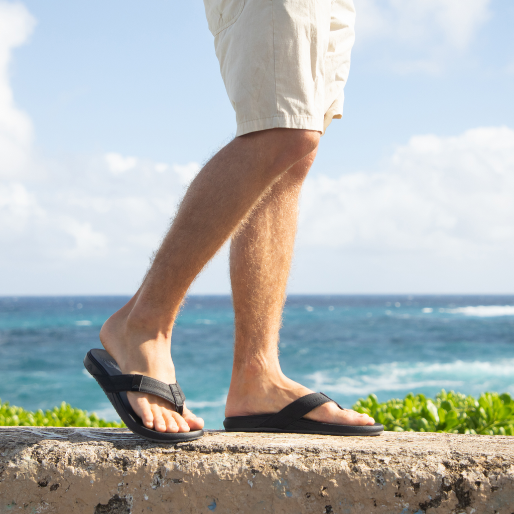 Side view of men's Cushion Phantom 2.0 flip flops on right foot by ocean, showing comfort and surf-inspired design.