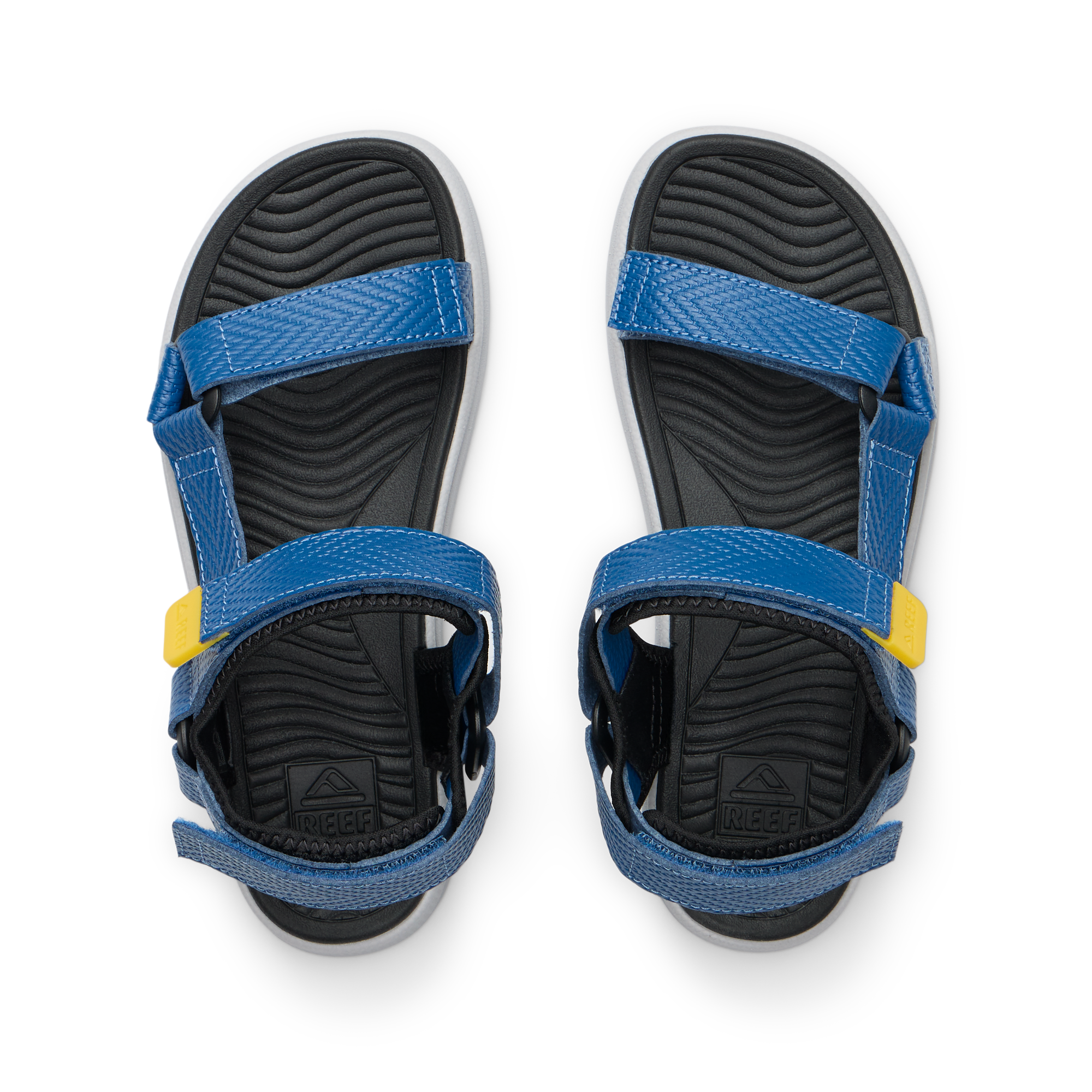 Kids Shoremazing sandals facing upward, blue straps with yellow details, black textured footbeds, beach-inspired comfort design.
