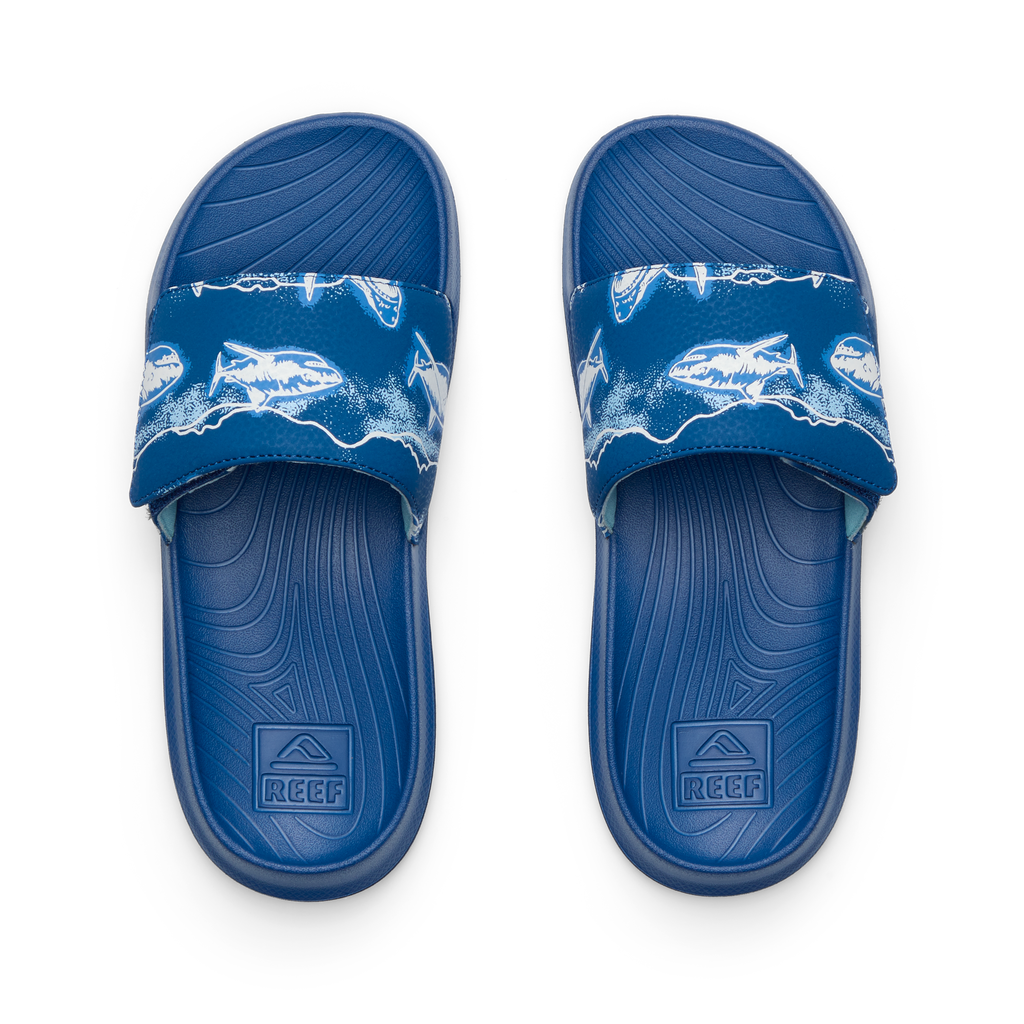 Top view of blue Kids Salty Slide facing up, featuring reef anatomical arch support and shark print strap for beach comfort.