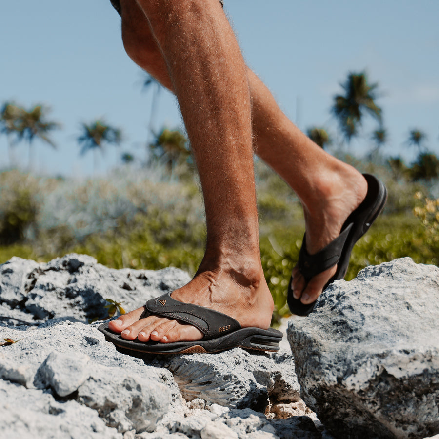 Close-up of a man's feet wearing black Fanning flip flops facing right, showcasing comfort and arch support for beach use.