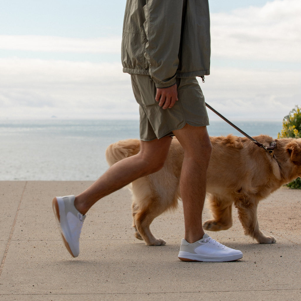 Man walking dog by the beach wearing Shoreline Del Mar sneakers facing right with white upper and brown sole