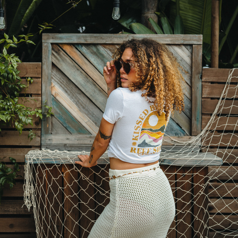 Woman wearing white Mika Sweater Skirt shown from back in stylish beach-inspired casual setting with greenery background