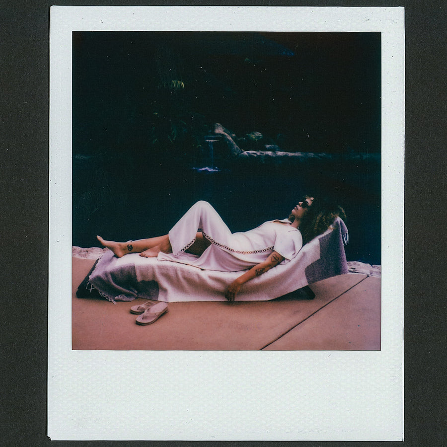Woman wearing Irina Shirt Dress reclining on lounge chair with sandals placed on ground by her feet, beach-inspired comfort style.
