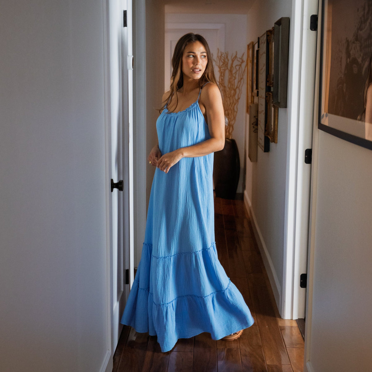 Woman wearing a light blue Lainey Maxi Dress standing in a hallway, showcasing its flowing beach-inspired design.