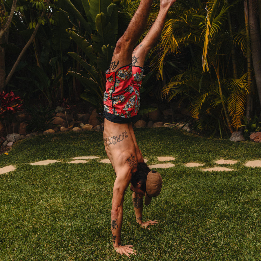Adult man wearing red Tanner Boardshorts doing a handstand outdoors, surf-inspired comfort and water-friendly design.