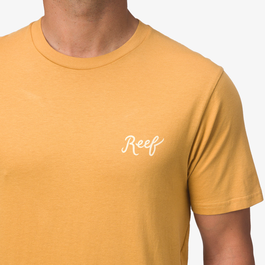 Close-up of the upper torso wearing a honey mustard Jacob Tee with Reef logo, highlighting comfort and beach-inspired style.