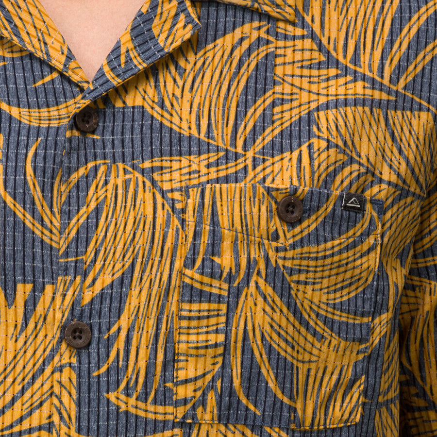 Close-up of men’s Kantis Shirt pocket and buttons with brown tropical leaf print on textured fabric, surf-inspired comfort.