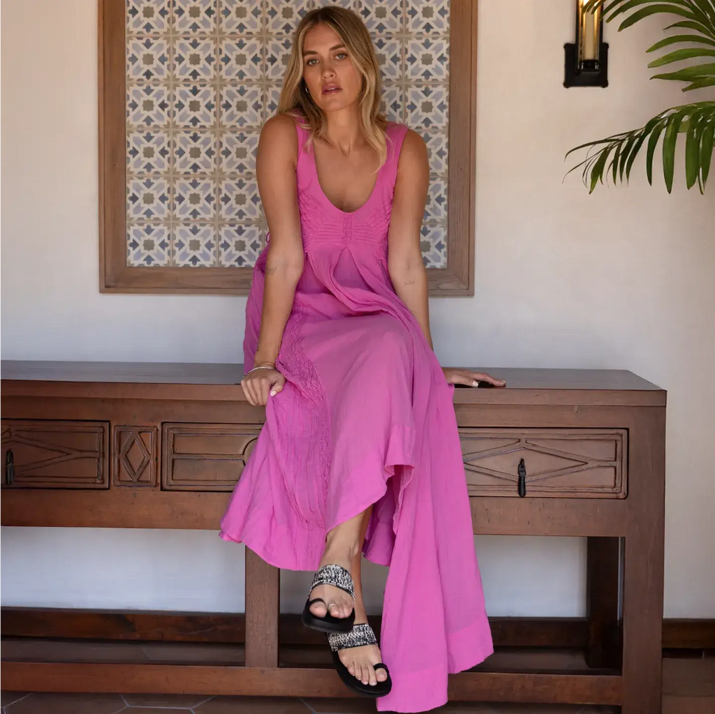 Woman wearing Flora Cruz black sandals facing forward, seated on wooden bench, showcasing comfort and beach-inspired style.