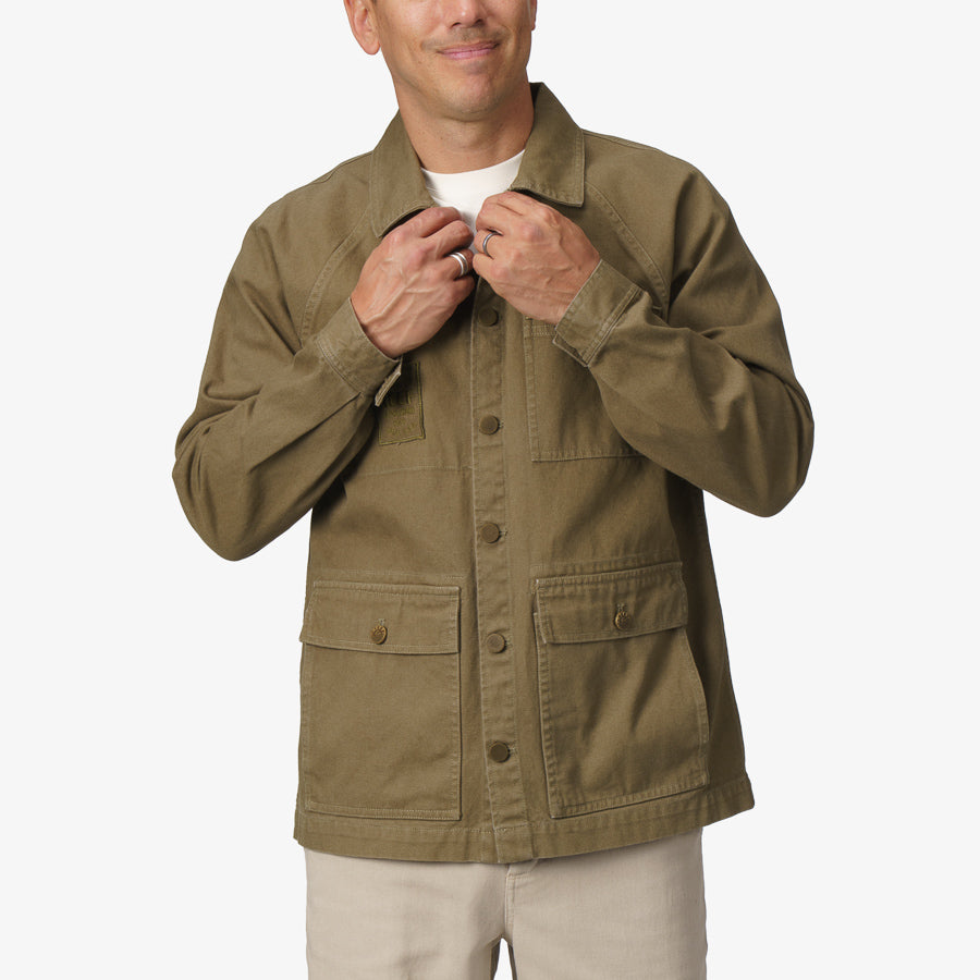 Front view of man adjusting collar wearing olive Landon Coat with button pockets, surf-inspired and durable fabric for comfort.