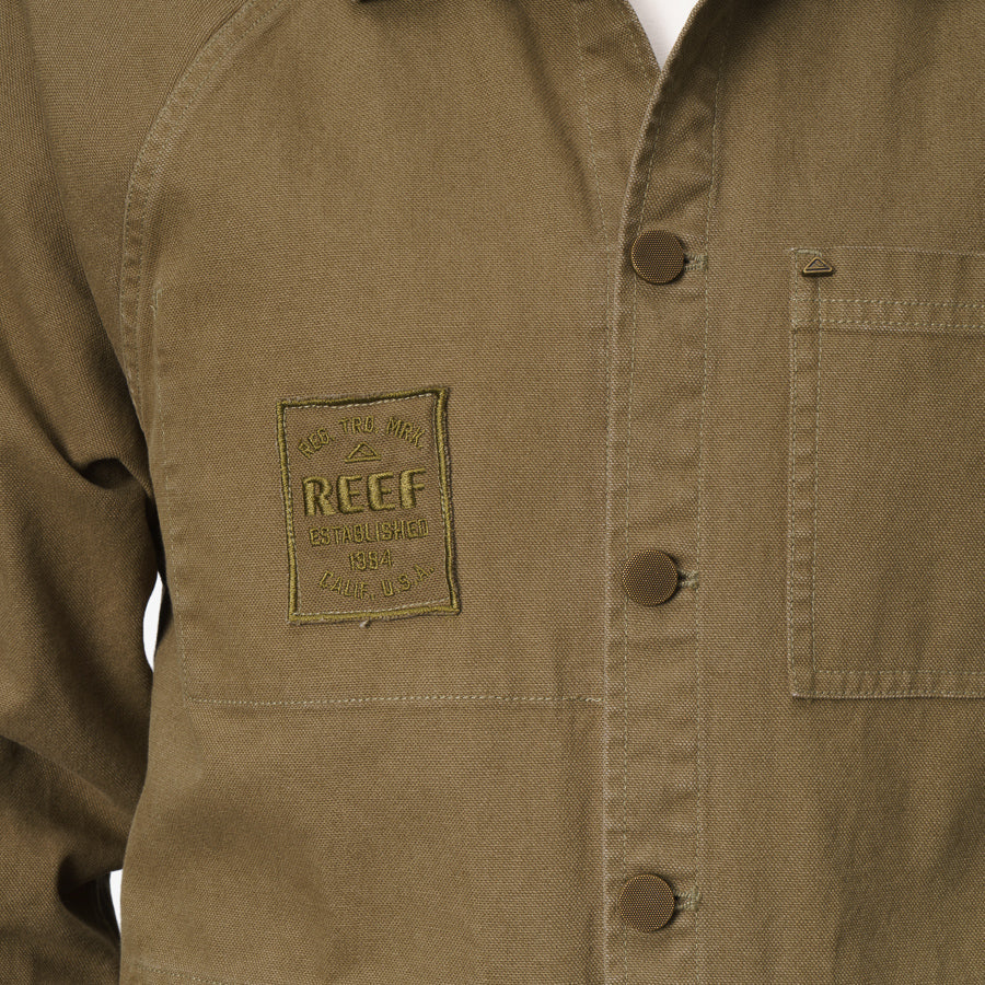 Close-up of the front left side of the Landon Coat showing buttons, chest pocket, and REEF logo patch in brown fabric.