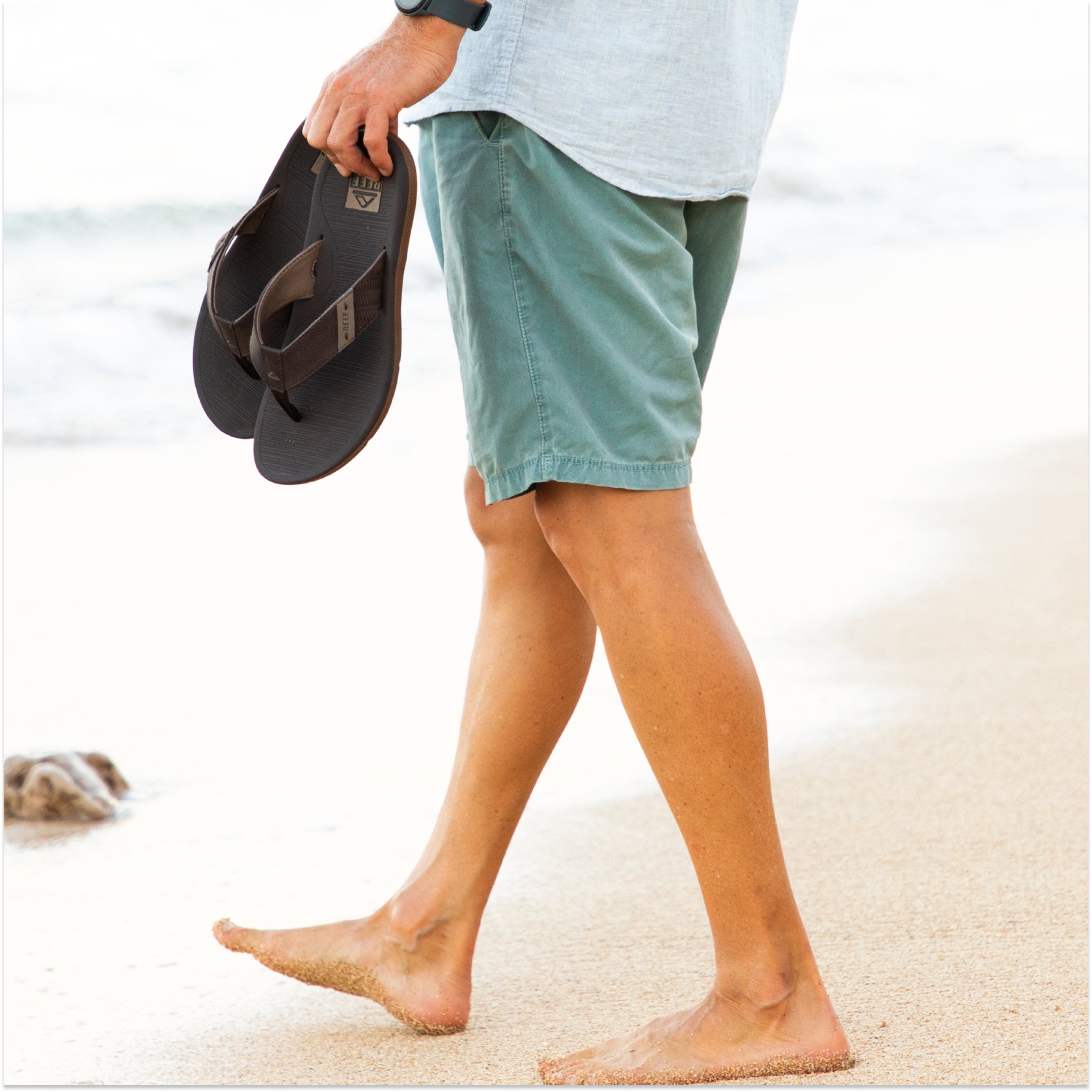 Man holding brown reef santa ana sandals on the beach