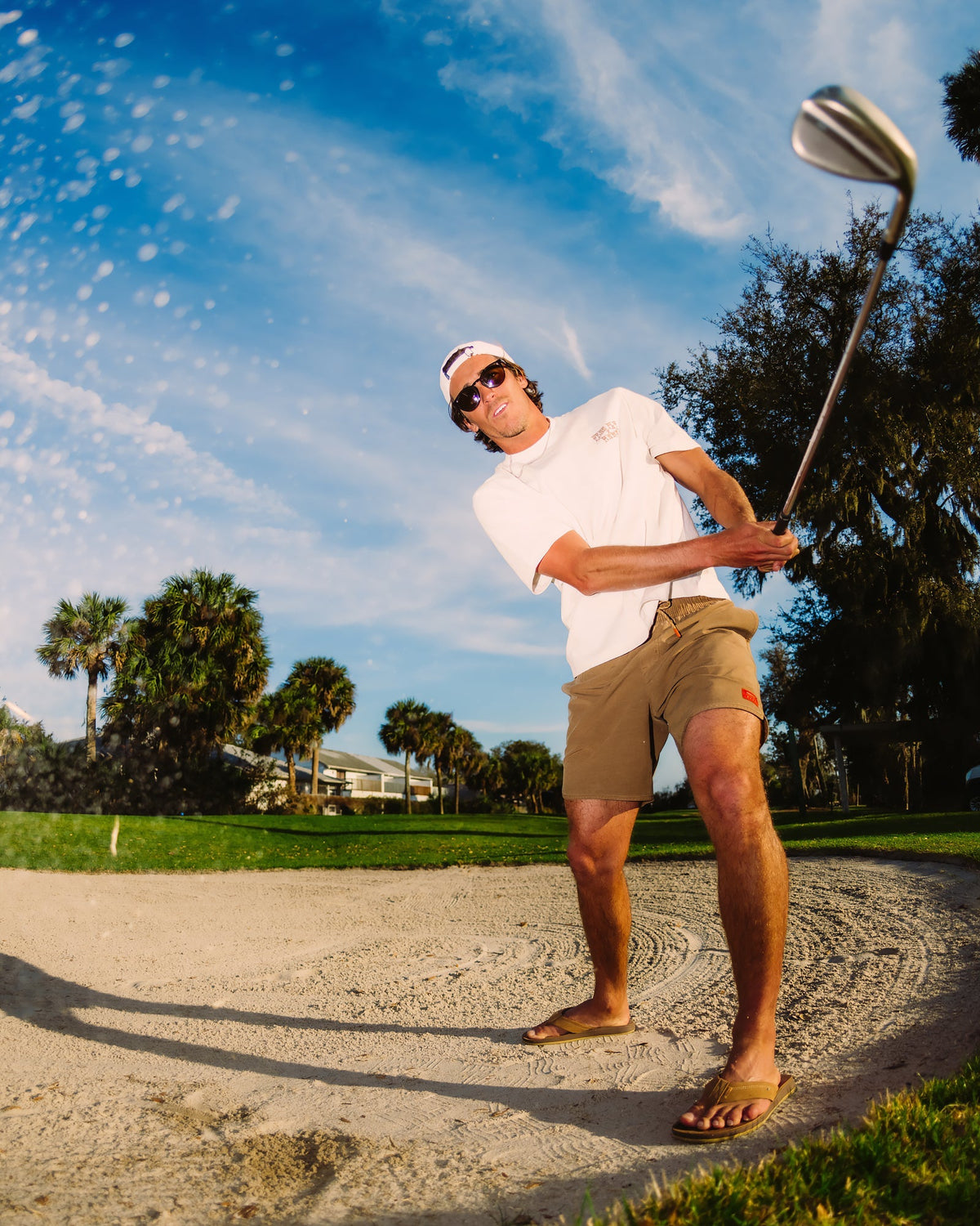 Man wearing Men's Reverb Short Unlined – 7" - Coconut in sandy bunker playing golf barefoot under clear sky