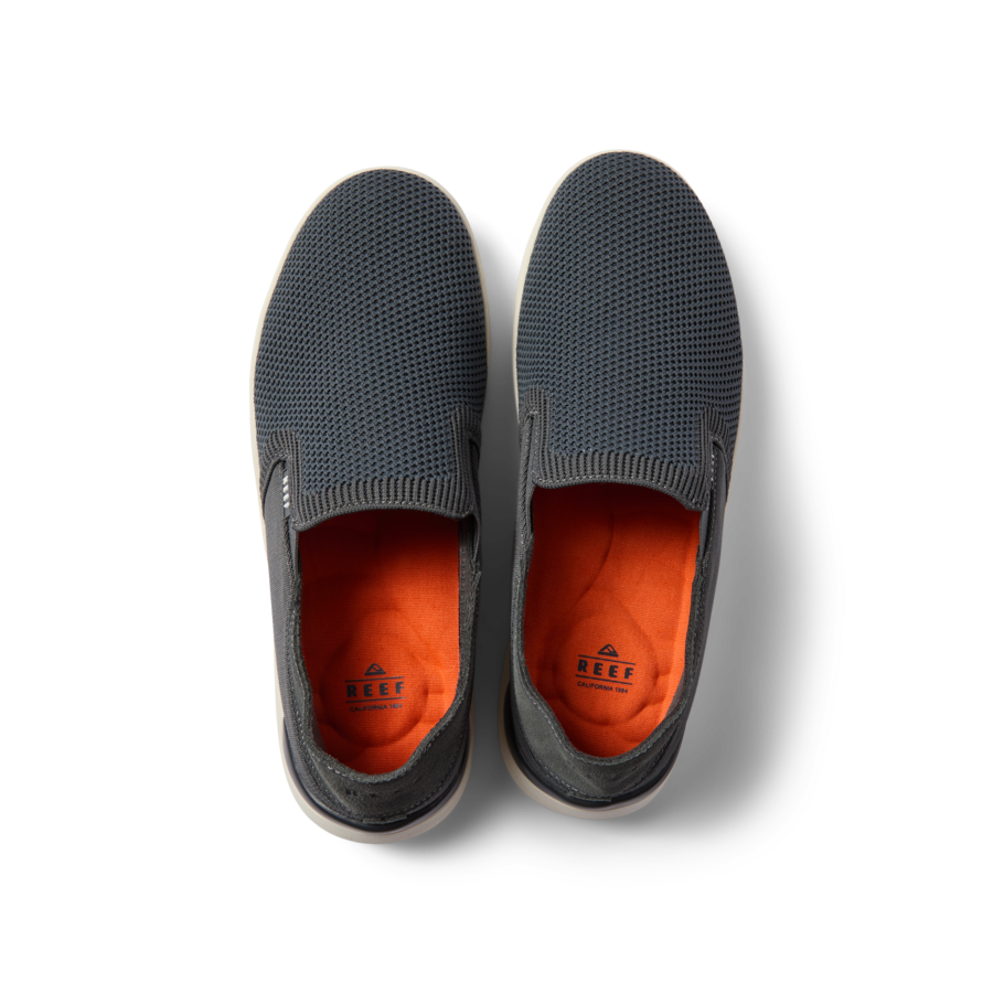 Top view of black and white Neptune Slip-On shoes with orange insoles, featuring breathable mesh and comfortable cushioning.
