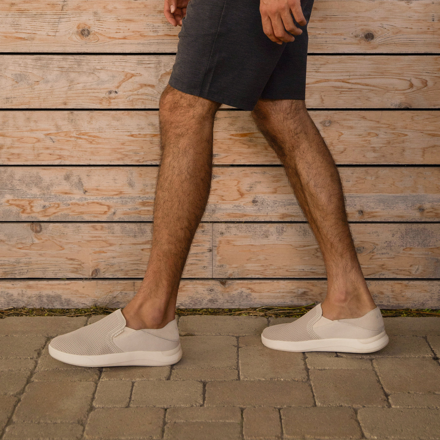 Men wearing tan Neptune Slip-On shoes walking right, side view showing shoe profile and upper mesh detail.