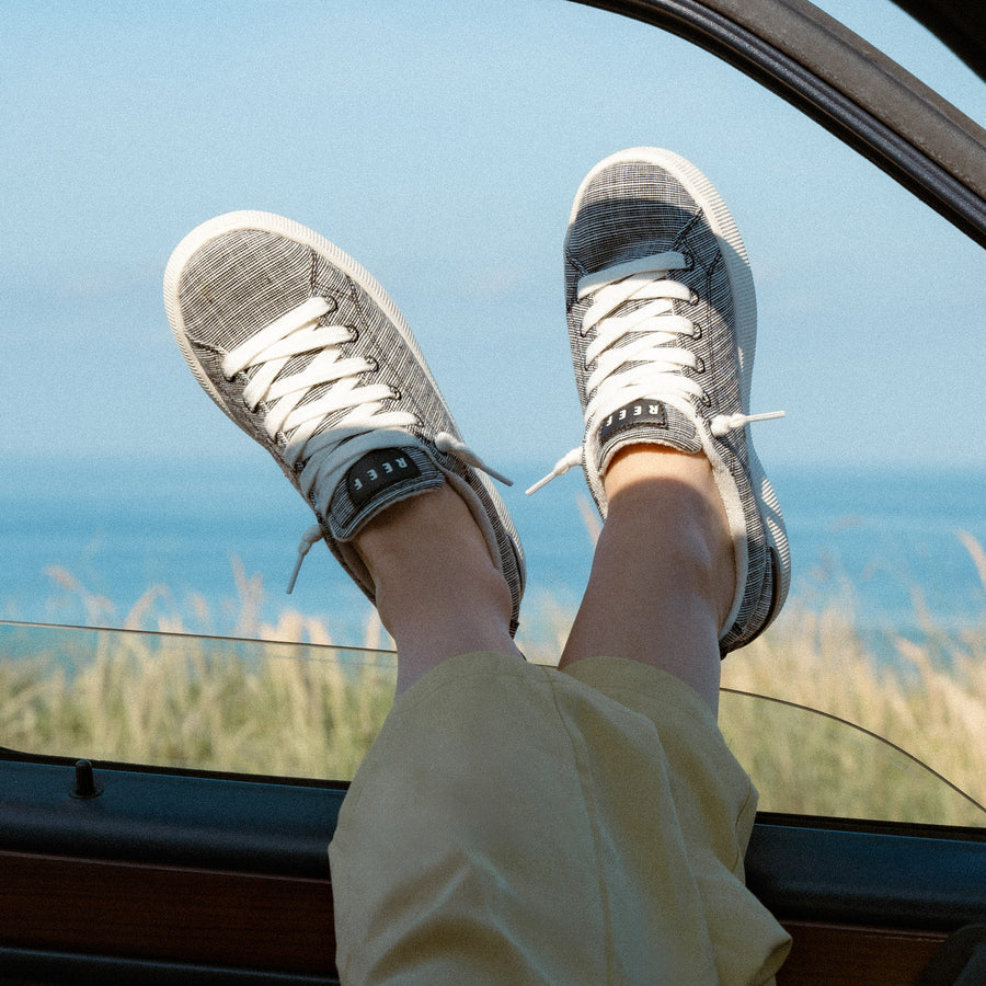 Pair of Neptune Alana sneakers facing forward, worn by a woman relaxing with feet out the car window by the beach.