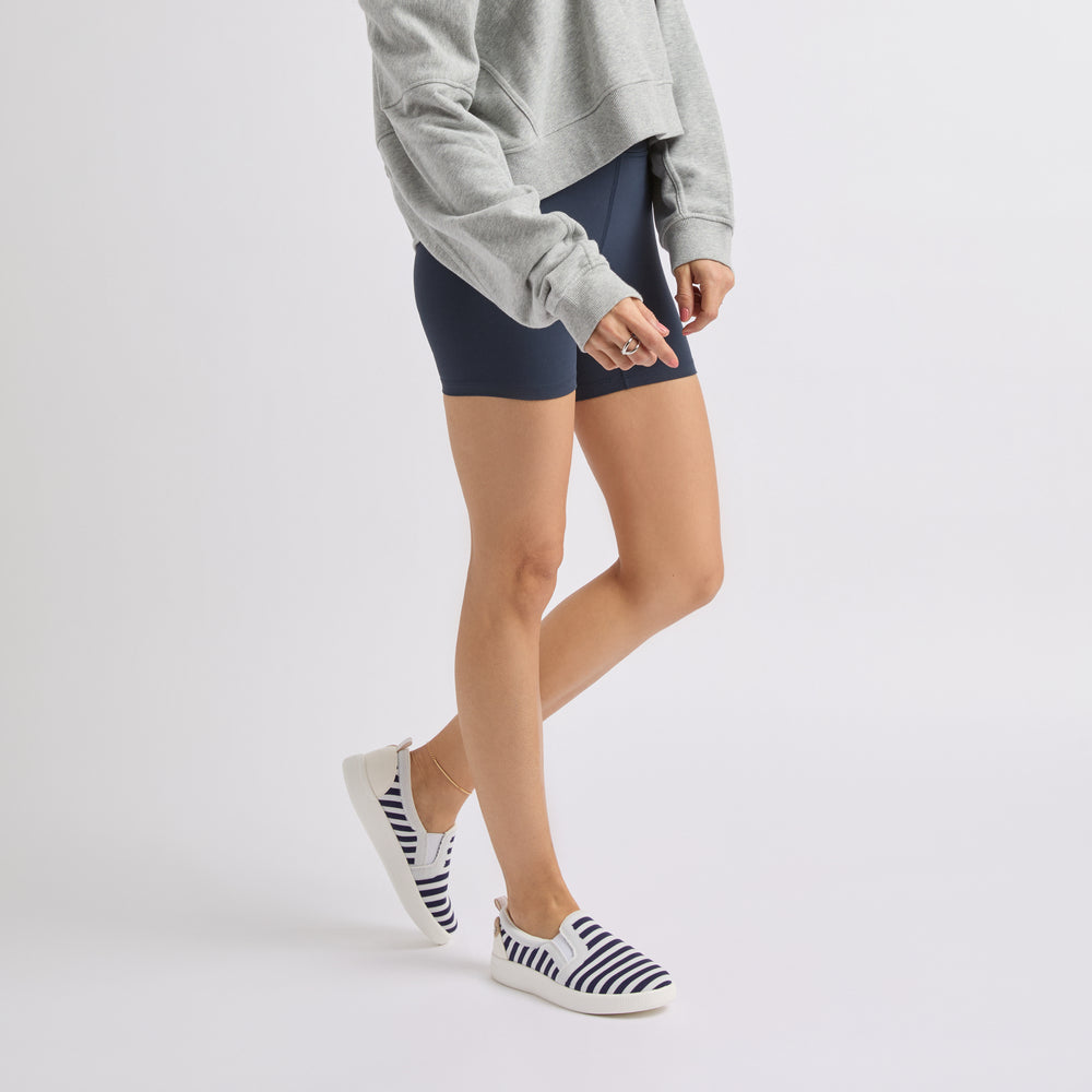 Woman wearing Neptune Elyse navy and white striped slip-on shoes facing left, side view showing shoe profile and comfort design.