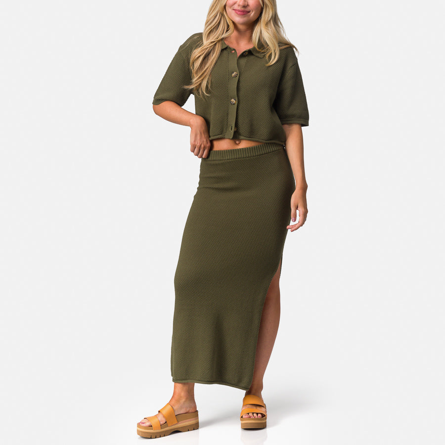 Woman wearing Up North Sweater Top in olive, front view, paired with a long skirt and tan sandals, beach-inspired comfort apparel.
