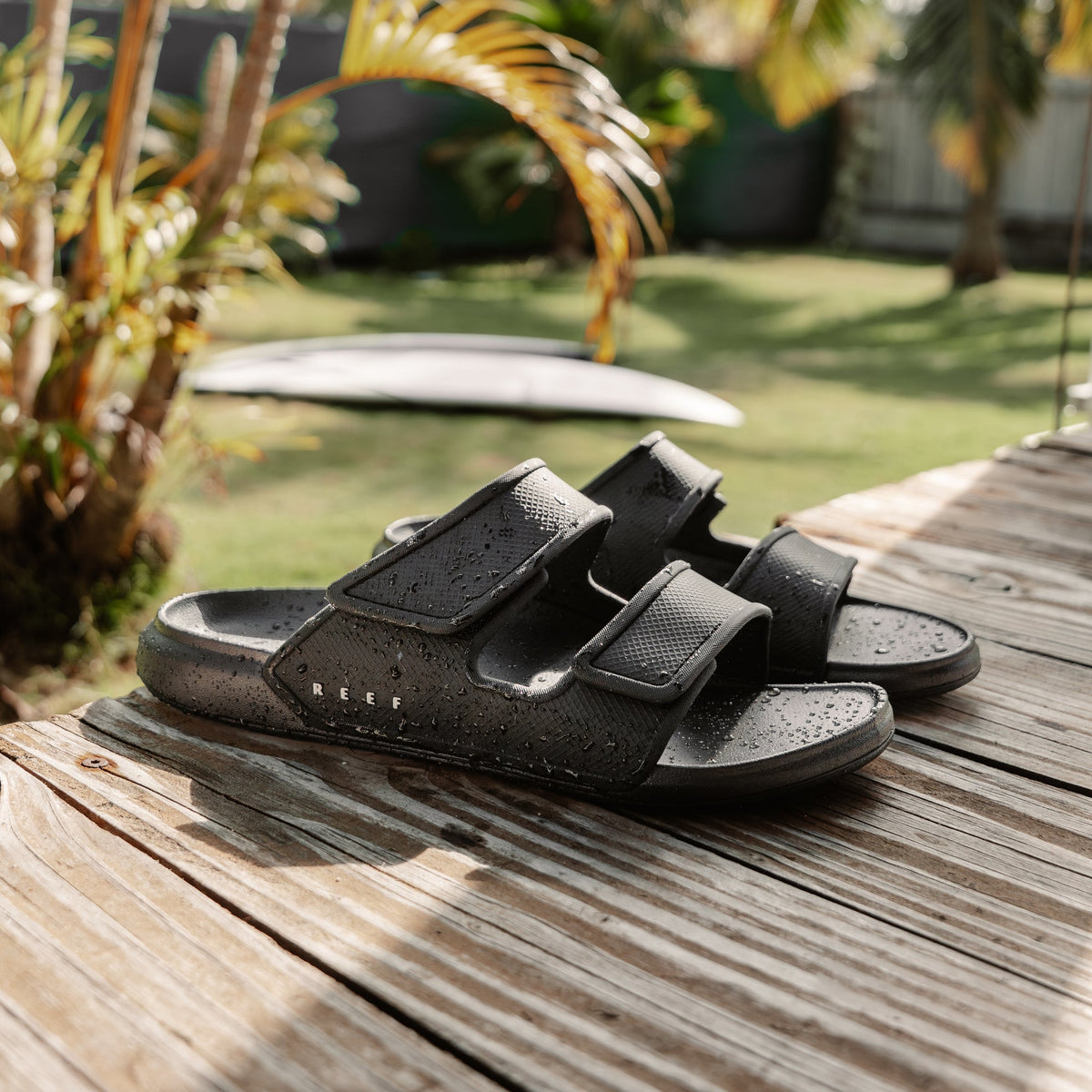 Oasis Adapt black men's sandals facing right with soft-rebound cushioning and anatomical arch support on wood deck.