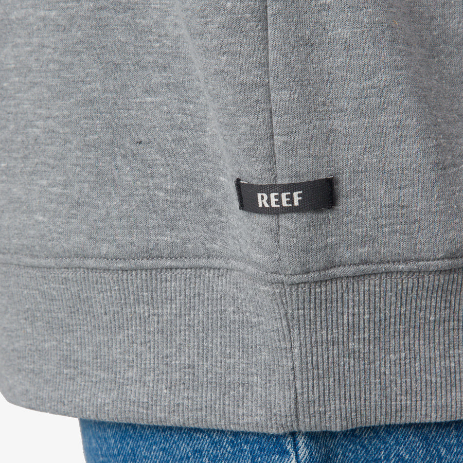 Close-up of the REEF tag on the gray hem of the Oversized Raglan Fleece for women, highlighting durable fabric.