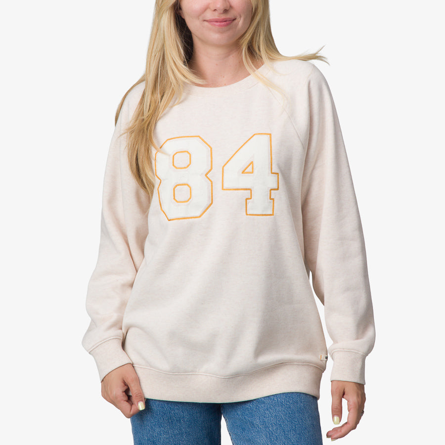 Woman wearing Oversized Raglan Fleece in oatmeal heather with orange 84 print, front view, surf-inspired comfort apparel.