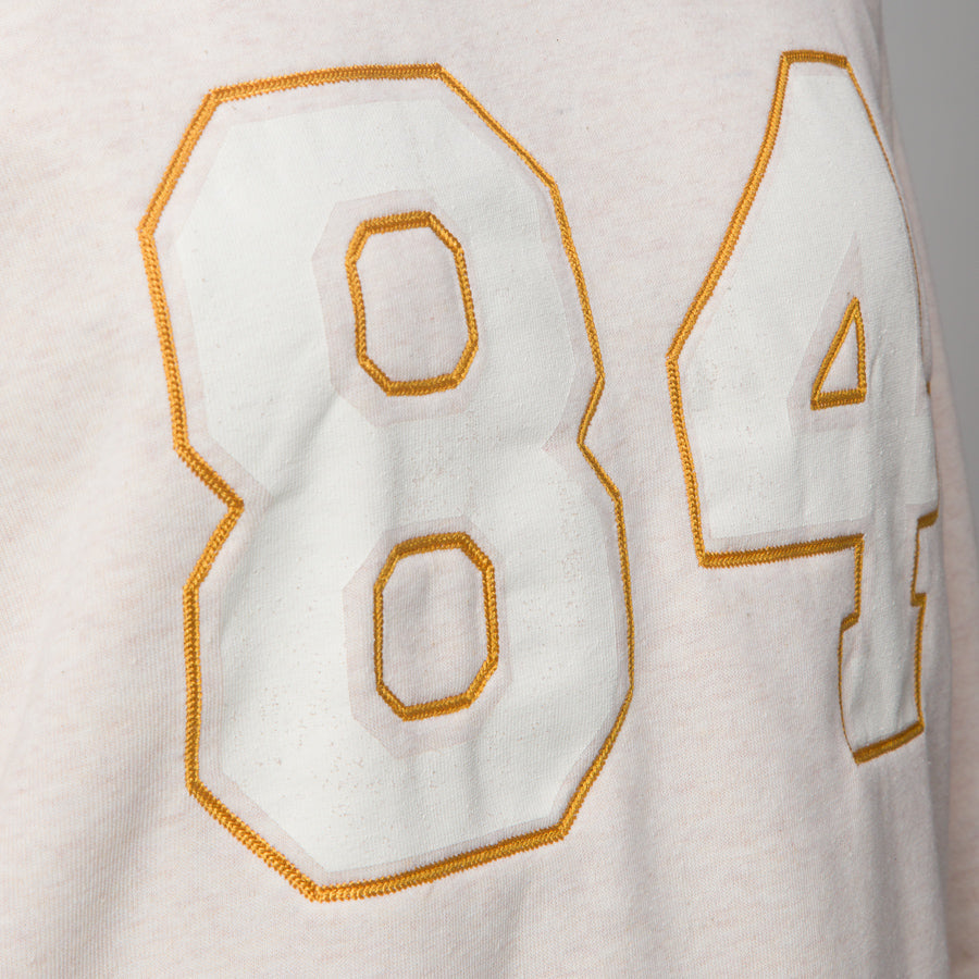 Close-up of oversized white and gold stitched numbers on front of women's Oversized Raglan Fleece, highlighting soft fabric texture.