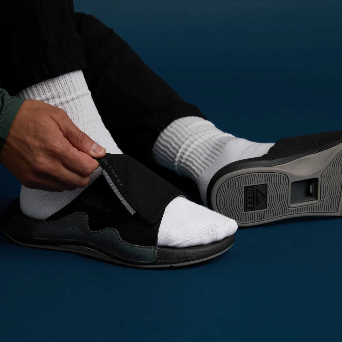 Black Cruiser Slide facing left with white socks, shown from side and bottom highlighting cushioning and arch support.
