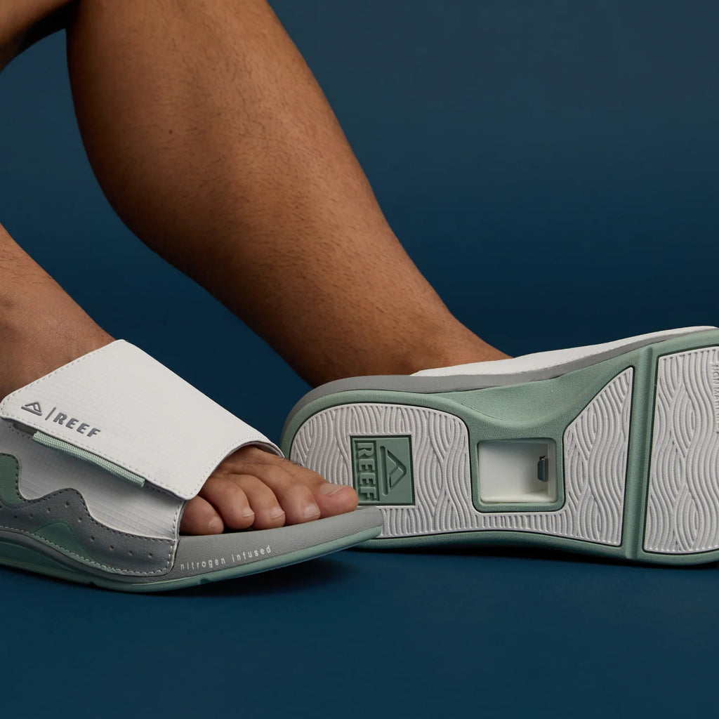 Feet wearing grey and white Cruiser Slide footwear, right foot sole facing forward showing tread and arch support design.