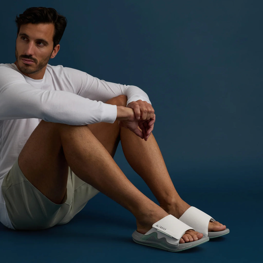 Man sitting wearing white Cruiser Slide sandals facing forward with arch support and cushioned footbed