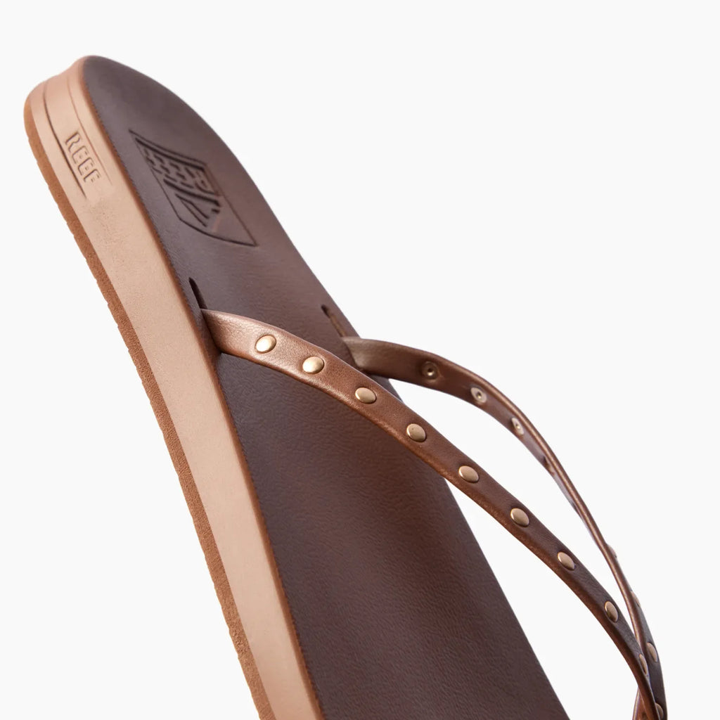 Close-up of the top and side of the right Cushion Slim Studs sandal in chocolate with studded straps facing up.