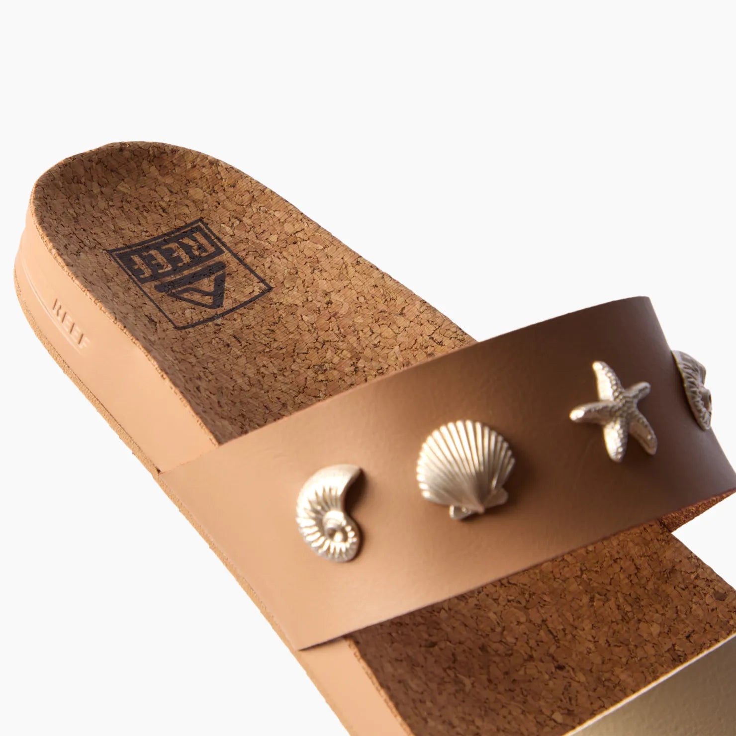 Cushion Vista women's tan sandal facing left, close-up of the front strap with seashell embellishments, beach-inspired comfort.