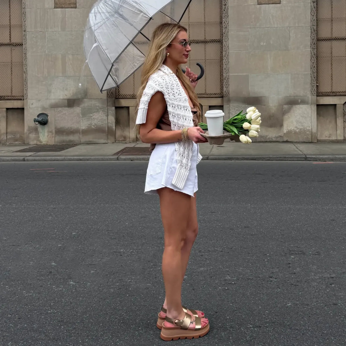 Side view of a woman wearing Vista Luxe Liah sandals with platform soles, holding white flowers and a coffee cup.