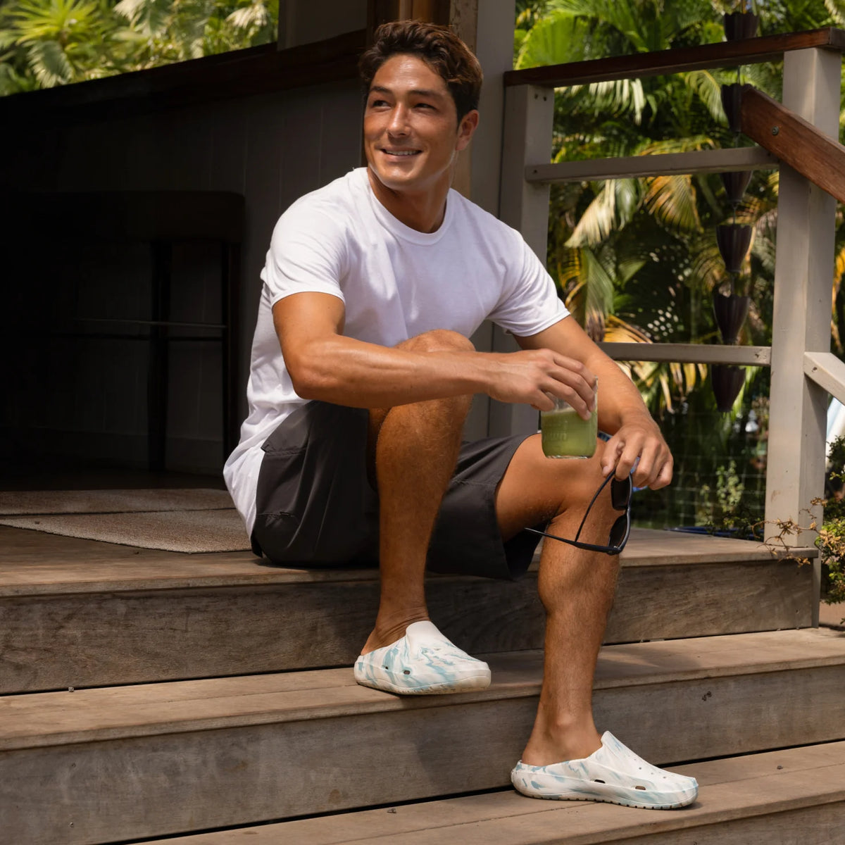 Glider shoes facing right on a man sitting on wooden steps, showing side and top with soft cushioning and arch support.