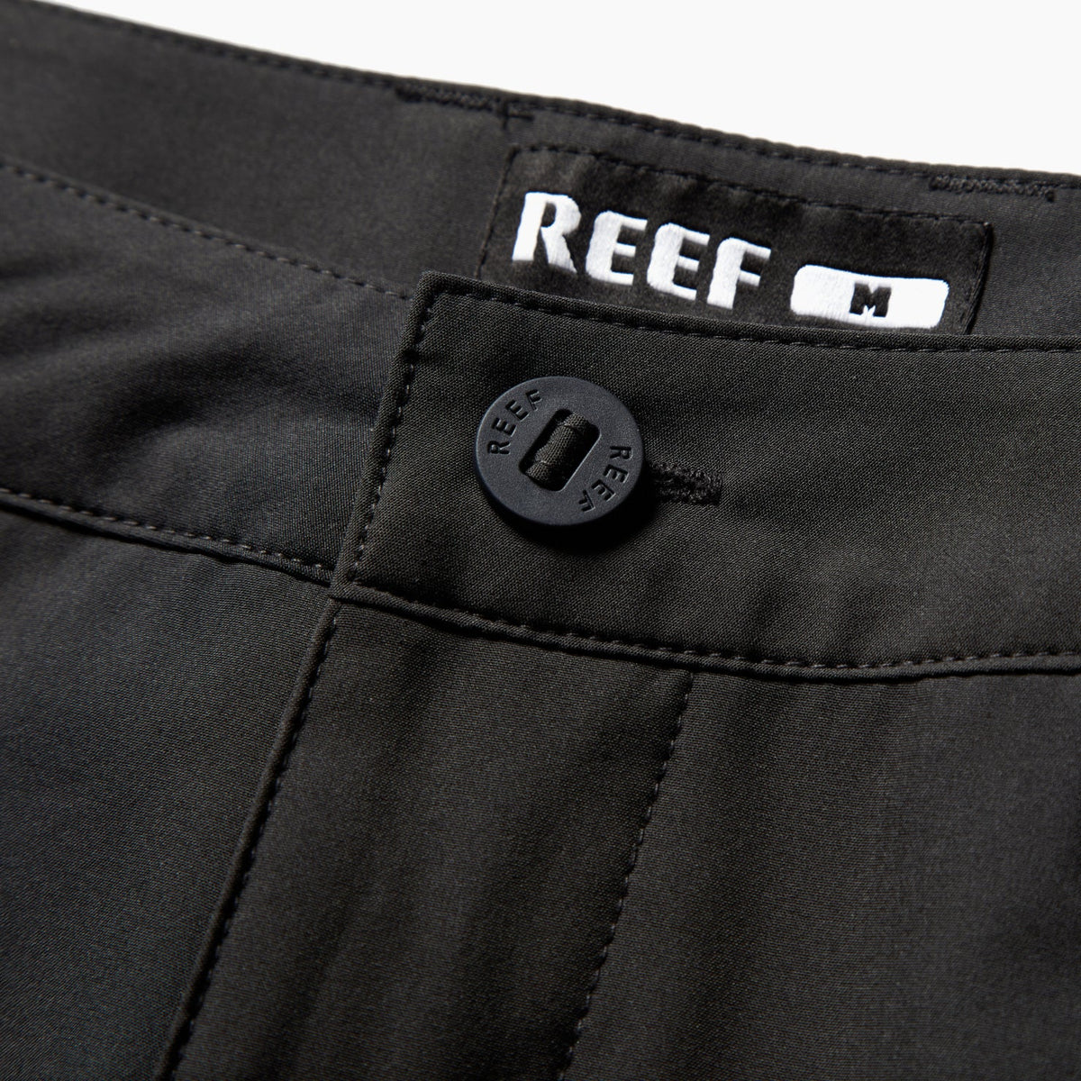 Close-up of the waistband and button on the black Dante Walk Short, featuring REEF branding and durable stitching.