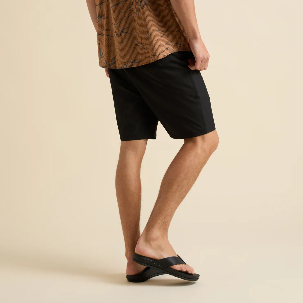 Rear view of man wearing black Dante Walk Short and black REEF sandals facing right, showcasing cushioned sole and arch support