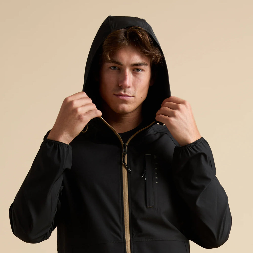 Man wearing a black Garvey Full Zip Jacket with hood up, front view showing front zipper and chest pocket details.