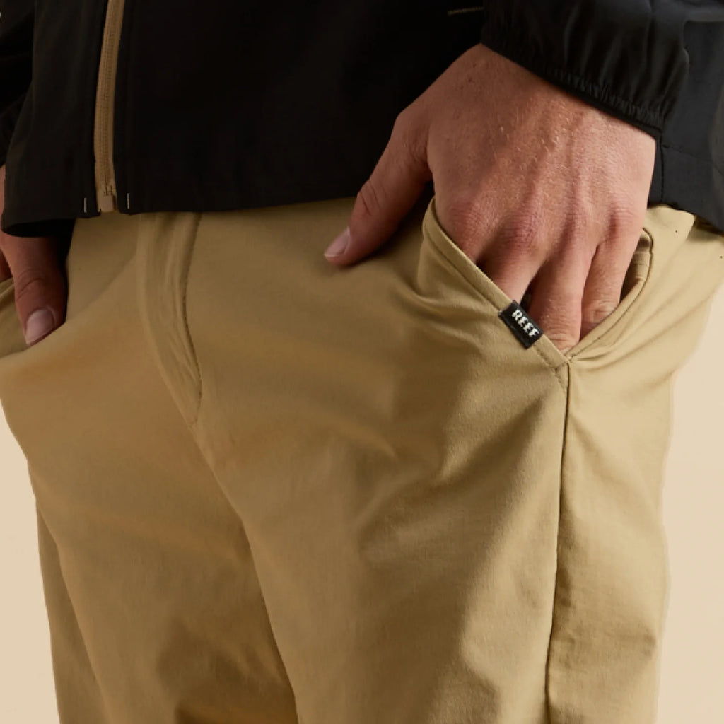 Close-up of a man's hand in the front pocket of tan Carrick Stretch Pant, showcasing comfort and stretch fabric.